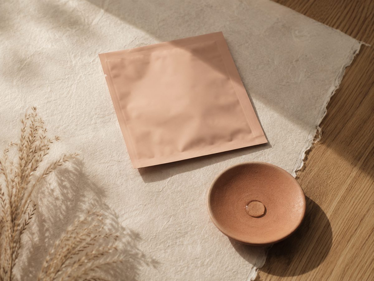 A folded peach-colored foil sheet mask on hanji paper next to a small terracotta ceramic dish.
